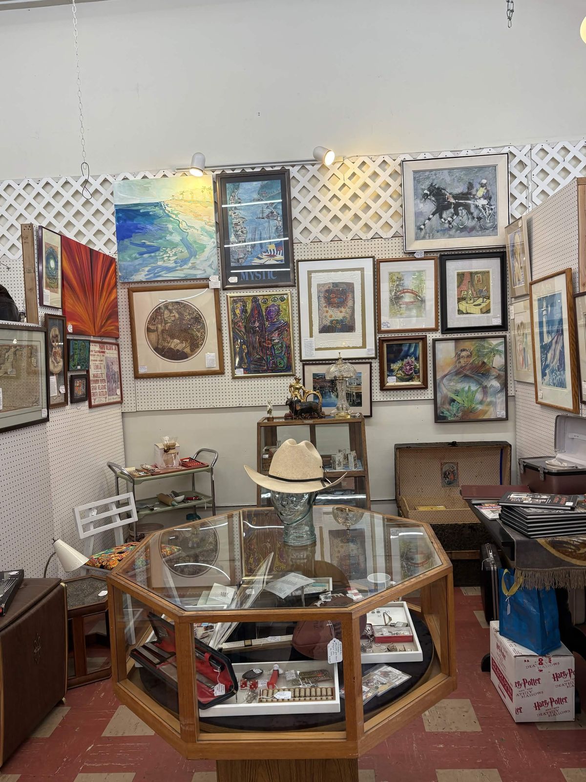 Art booth with pegboard walls covered in framed original paintings and a glass jewelry case
