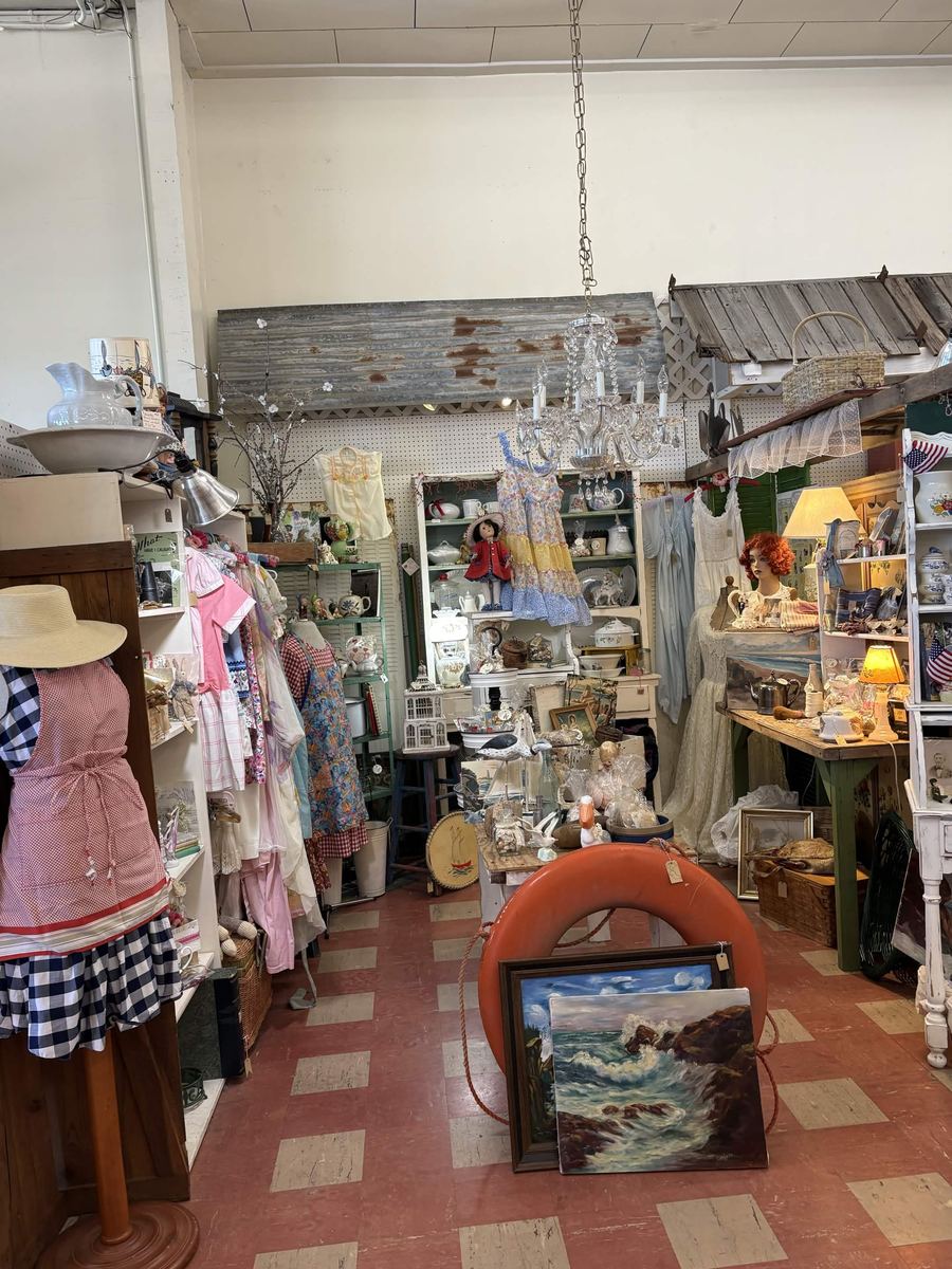 Cottage style booth with hanging aprons, lace dresses, a chandelier, and a life ring