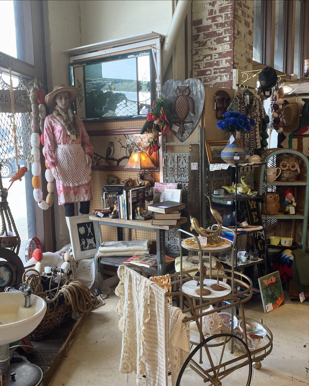 Cottage style booth with an apron dress on a mannequin, owl decor, and a bar cart