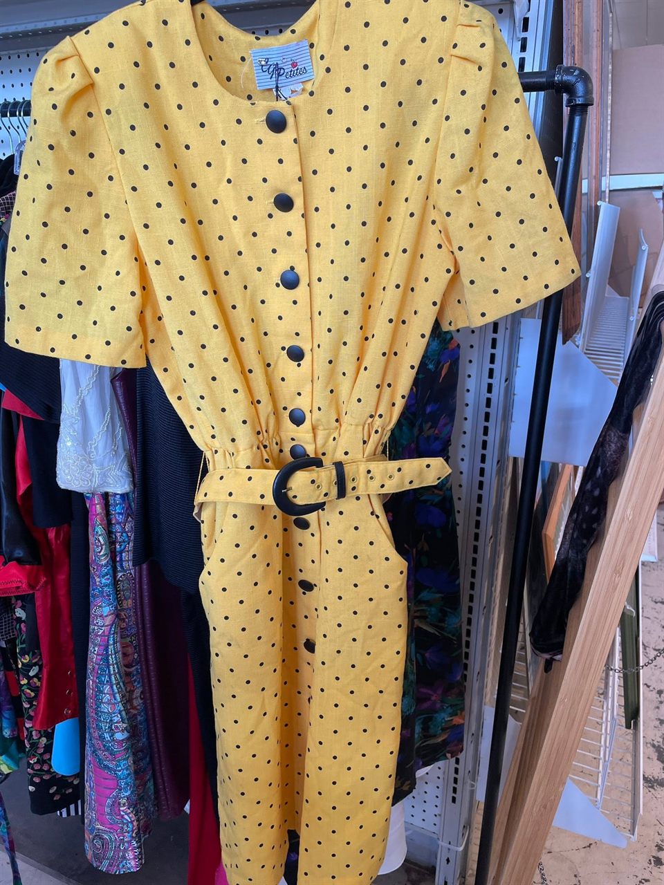 Yellow polka dot vintage dress with a belt on a clothing rack