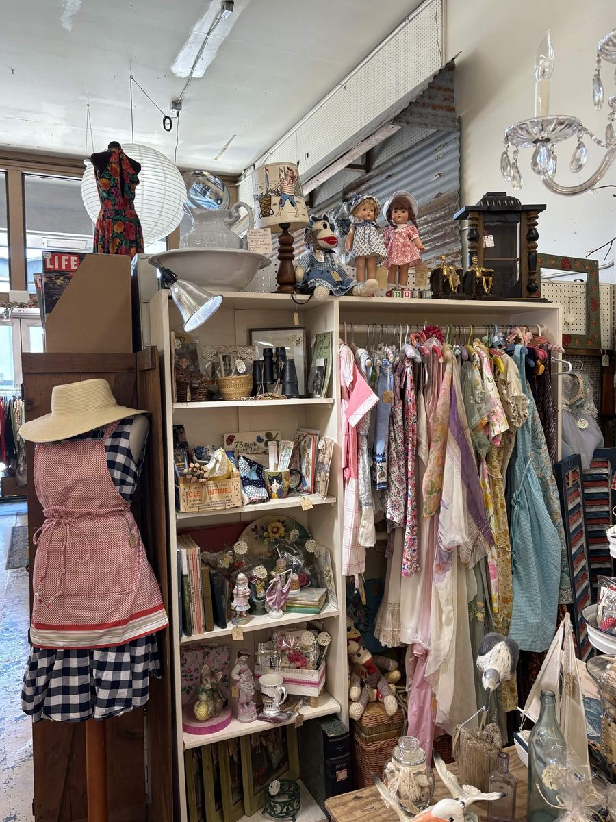 Booth with a rack of vintage dresses and aprons and old dolls