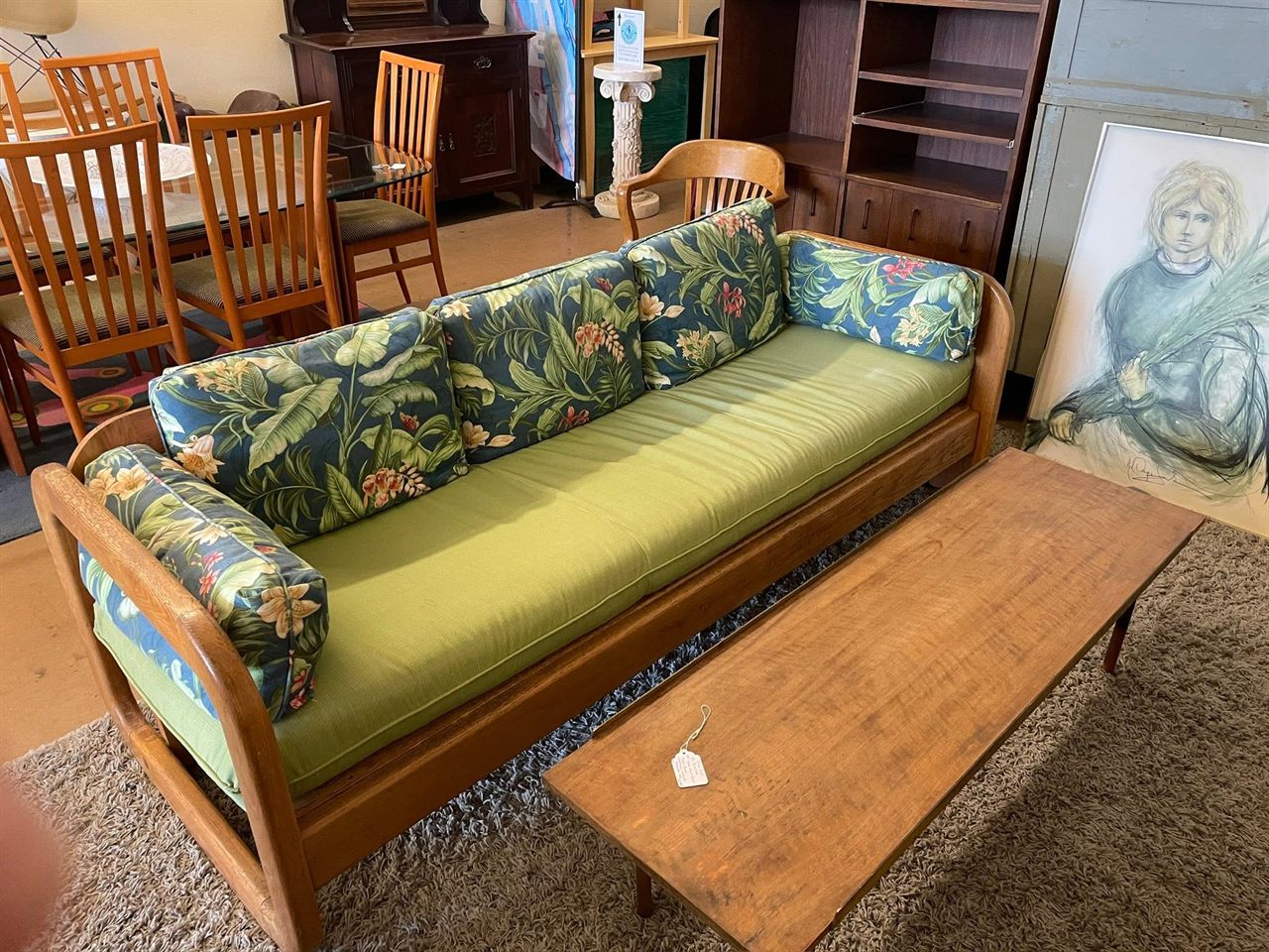 Mid-century wood frame sofa with green cushions and tropical print pillows