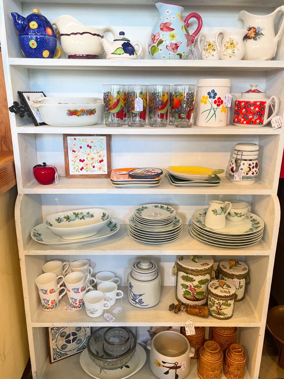 White hutch filled with vintage pitchers, Pyrex, dishes, mugs, and canisters