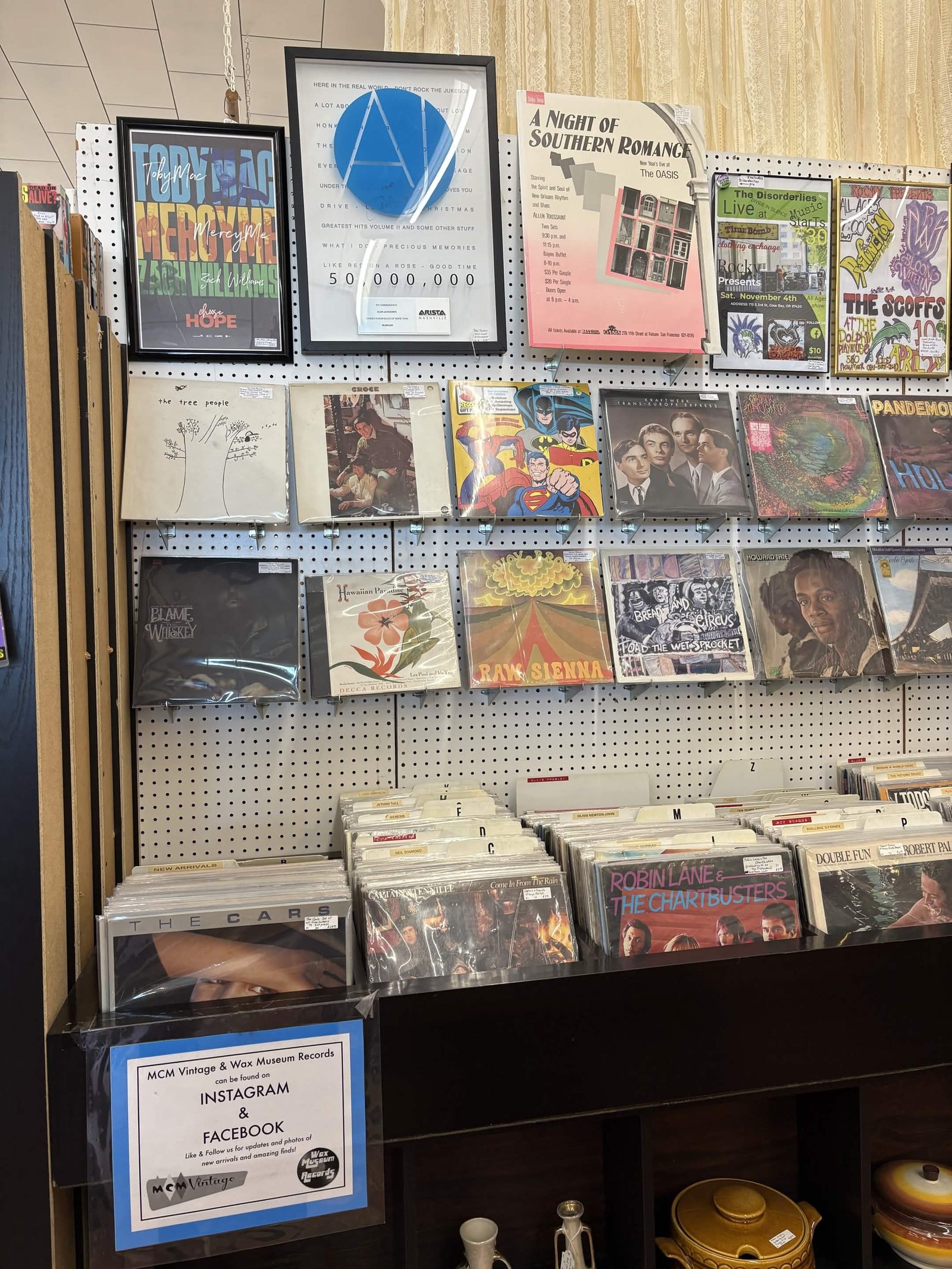 Wall of vinyl records in flip bins with framed album covers and local show flyers above